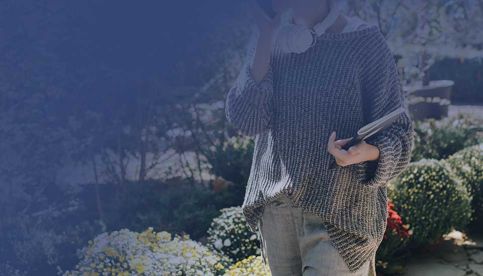 kvinna går med telefon och block under armen i en trädgård